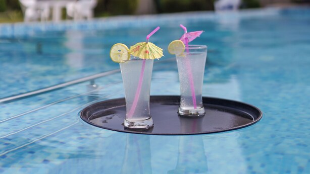 Una piscina amb dos gots d'una beguda transparent, cadascun decorat amb una làmina de llimona i una canya.