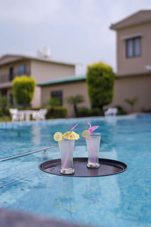 A swimming pool with two glasses of a clear beverage, each garnished with a slice of lemon and a straw. - Corbett Jungle Resort (Ramnagar)