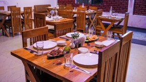 Zona de menjador amb taules i caires de fusta, plats, coberts i un petit arranjament floral al centre.