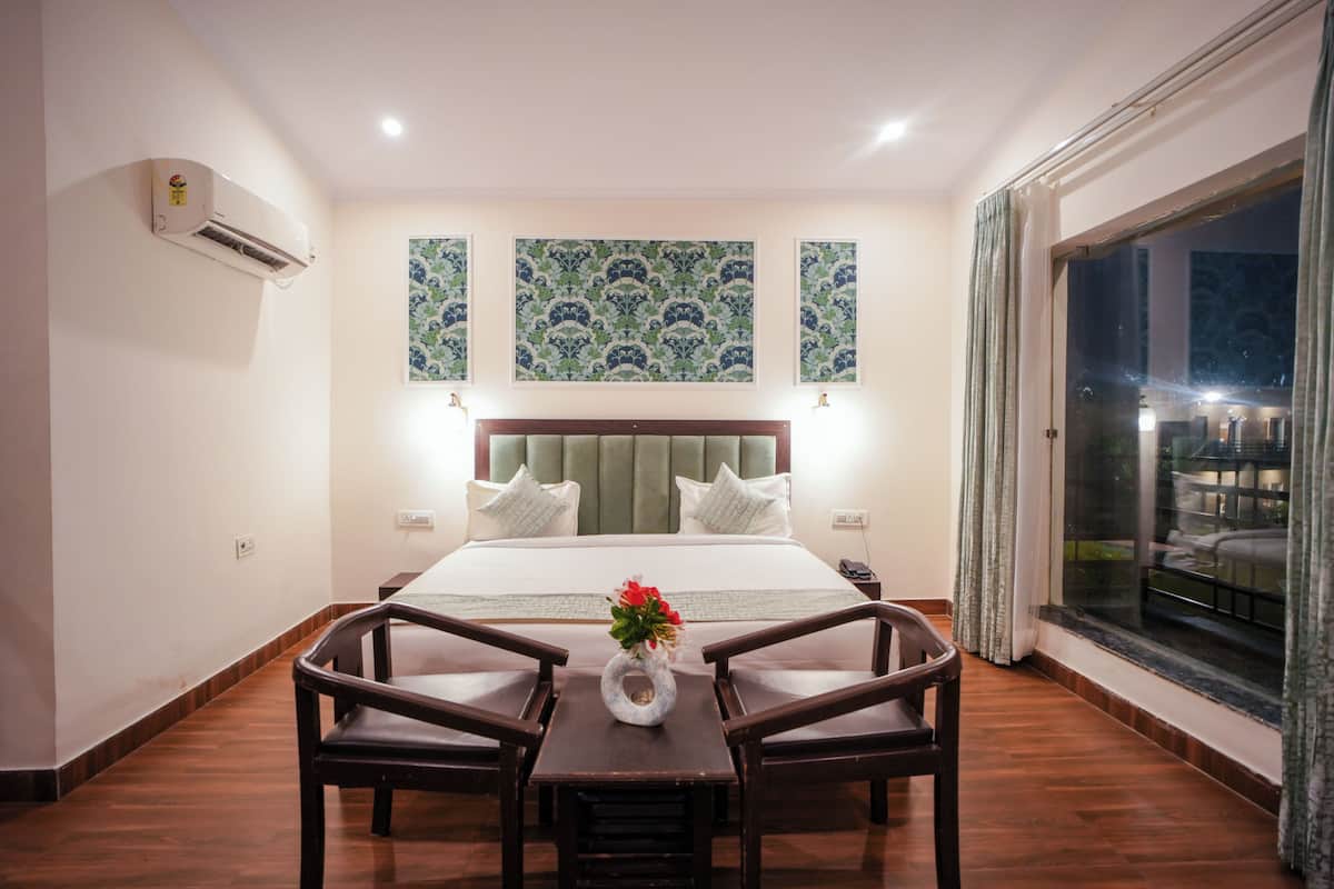 Habitación de hotel con cama, mesa con sillas, un jarrón con flores y un ventanal con cortinas.