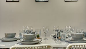 A dining table set with plates, bowls, and glasses, with framed botanical prints on the wall. - Chester Road Cozy House in Manchester (Manchester)