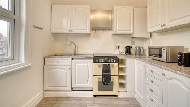 A kitchen with white cabinets, a stove, a microwave, and a coffee maker. - Chester Road Cozy House in Manchester (Manchester)