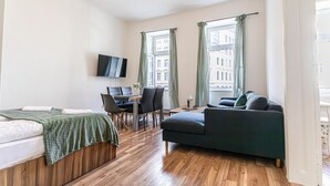 Une pièce comprenant un lit, un canapé, un bureau avec une chaise, une télévision et de grandes fenêtres avec des rideaux.
