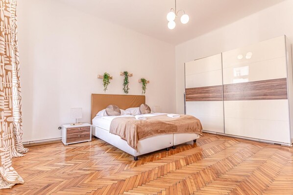 Une chambre à coucher comprenant un lit, des tables de chevet, une armoire et un parquet à motifs en chevrons.