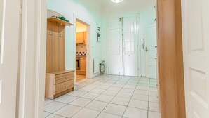 Un couloir avec une armoire en bois, une porte blanche et une cuisine visible au fond.