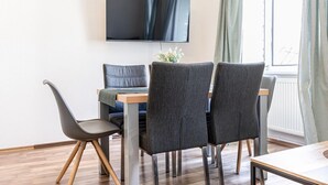 Une chambre moderne dotée d’un téléviseur à écran plat fixé au mur, d’une table à manger avec quatre chaises et d’une fenêtre avec des rideaux.