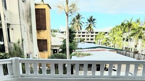 A balcony with a white railing, tiled floor, and a view of buildings and palm trees in the background.