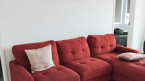A red sectional sofa with two pillows, a white abstract painting on the wall, and a doorway leading to another room.