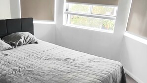 A bedroom with a bed, a headboard, and a window with blinds.