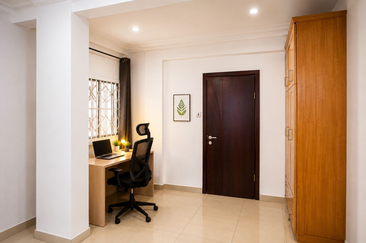 A room with a desk, chair, laptop, potted plants, a framed picture, and a wardrobe.