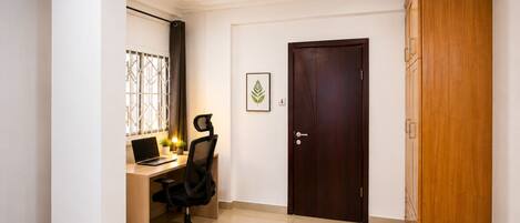 A room with a desk, chair, laptop, potted plants, a framed picture, and a wardrobe.