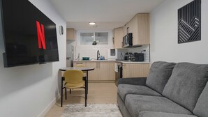 A compact living space with a kitchenette, a sofa, a chair, and a flat-screen TV mounted on the wall. - Modern Suite 2 by Royal Alex Hospital, LRT, Rogers| Free WiFi, Parking & Netflix (Edmonton)