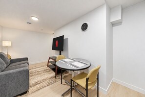A modern living room with a round table, two chairs, a sofa, a flat-screen TV, and a lamp.