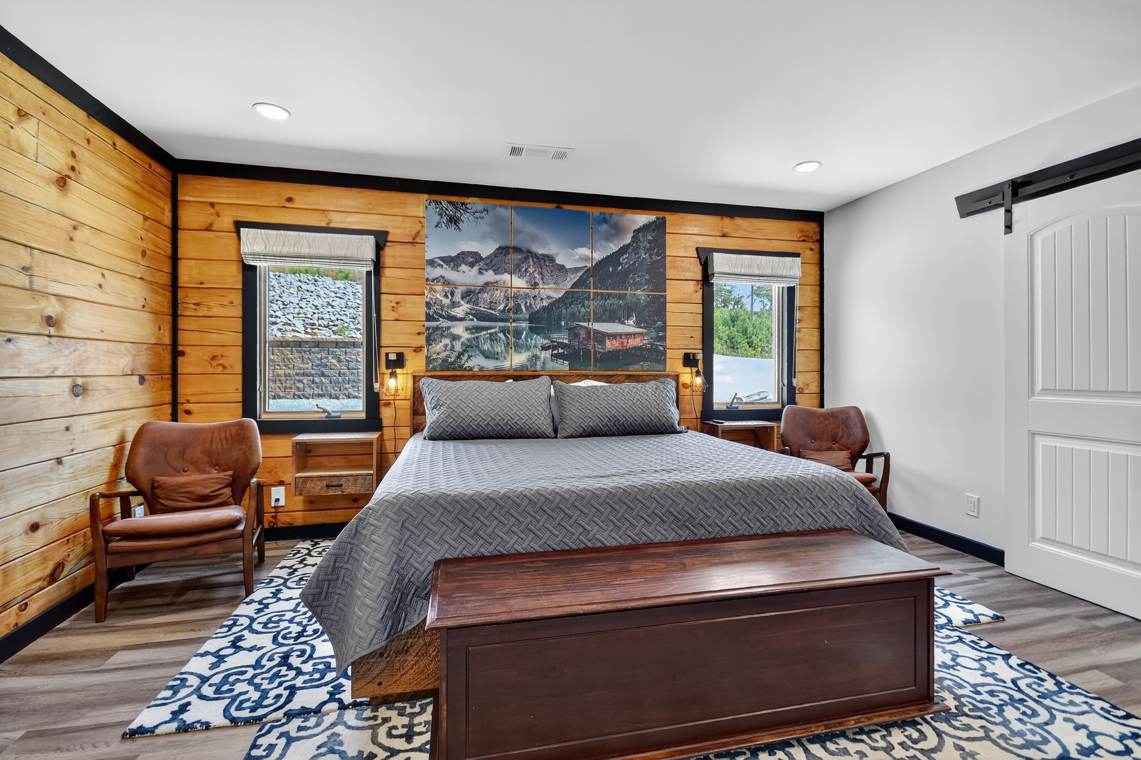 Camera da letto con un letto grande, pareti in legno, due finestre e vista sulle montagne.