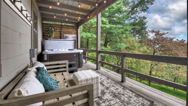 A cozy outdoor deck with a hot tub, wooden furniture, and a view of a forest. - Gorgeous mountain view cabin rental, hot tub, firepit, WiFi, pet-friendly (Ellijay)