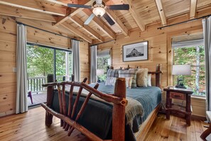 Une chambre dans une cabane en bois, avec un lit, un banc en bois, un ventilateur de plafond et de grandes fenêtres.