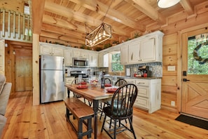A wooden cabin interior with a kitchen, dining area, and a bench.