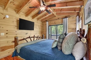 A wooden cabin bedroom with a bed, pillows, a ceiling fan, and a window.