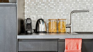 A modern kitchen with grey cabinetry, a tiled backsplash, a kettle, a coffee maker, and jars of pasta.