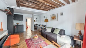 A modern living room with a wooden ceiling, a grey sofa, a glass coffee table, and a red rug.