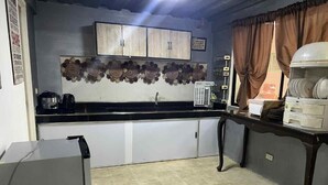 Eine kleine Küche mit Kühlschrank, Kaffeemaschine und Spüle. Darüber hängt ein dekoratives Wandbild und darüber befindet sich ein Schrank mit einer Mikrowelle.