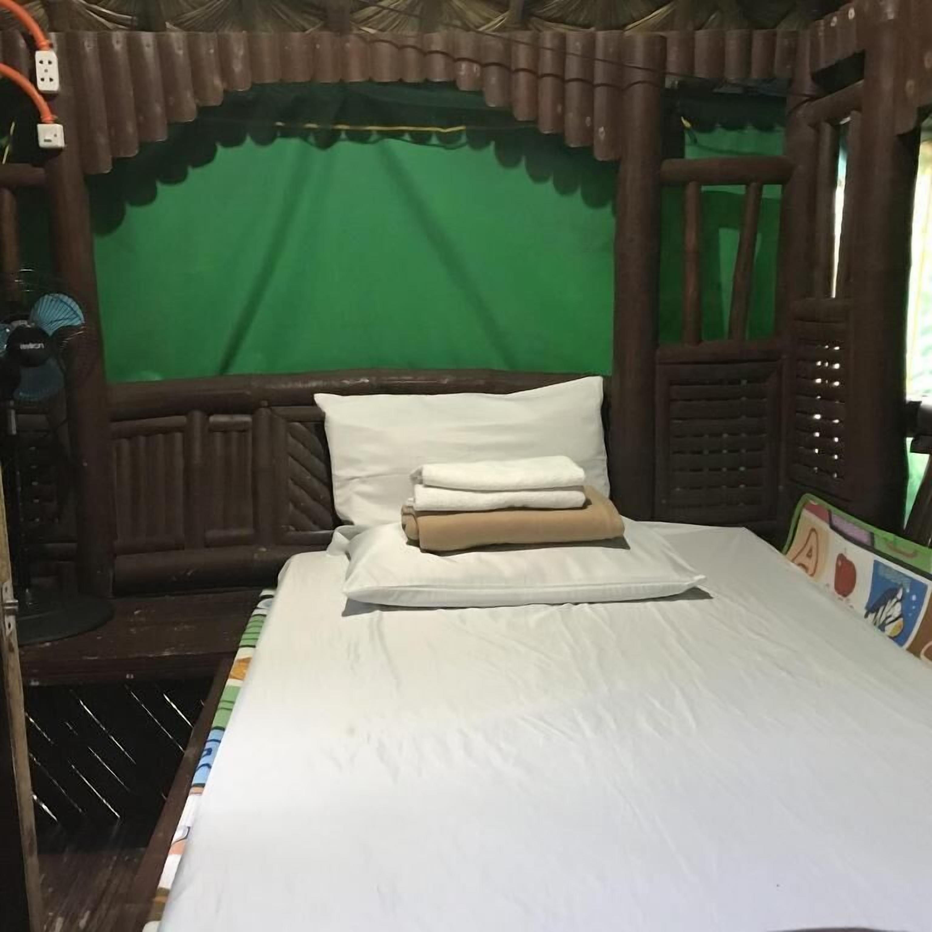 A wooden bed with white bedding, a green curtain, and a small window with a view of greenery.