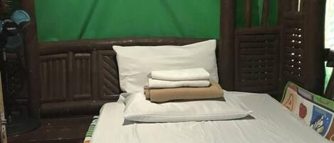 A wooden bed with white bedding, a green curtain, and a small window with a view of greenery.