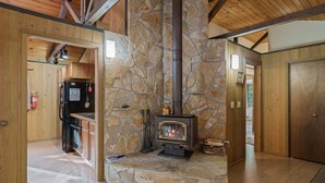 Una chimenea de piedra con estufa de leña, vigas de madera y una cocina con electrodomésticos.