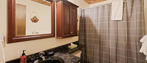 A bathroom with a black sink, a mirror, wooden cabinets, a shower curtain, and a towel hanging on the wall.
