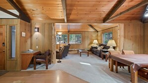 Interior acogedor de una cabaña con piso de madera, un sofá, una mesa de centro, un escritorio con silla y una chimenea.