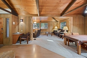 A cozy cabin interior with a wooden floor, a sofa, a coffee table, a desk with a chair, and a fireplace. - 7 Bobcat - Hot Tub, SHARC, Close to Village, A/C (Sunriver)