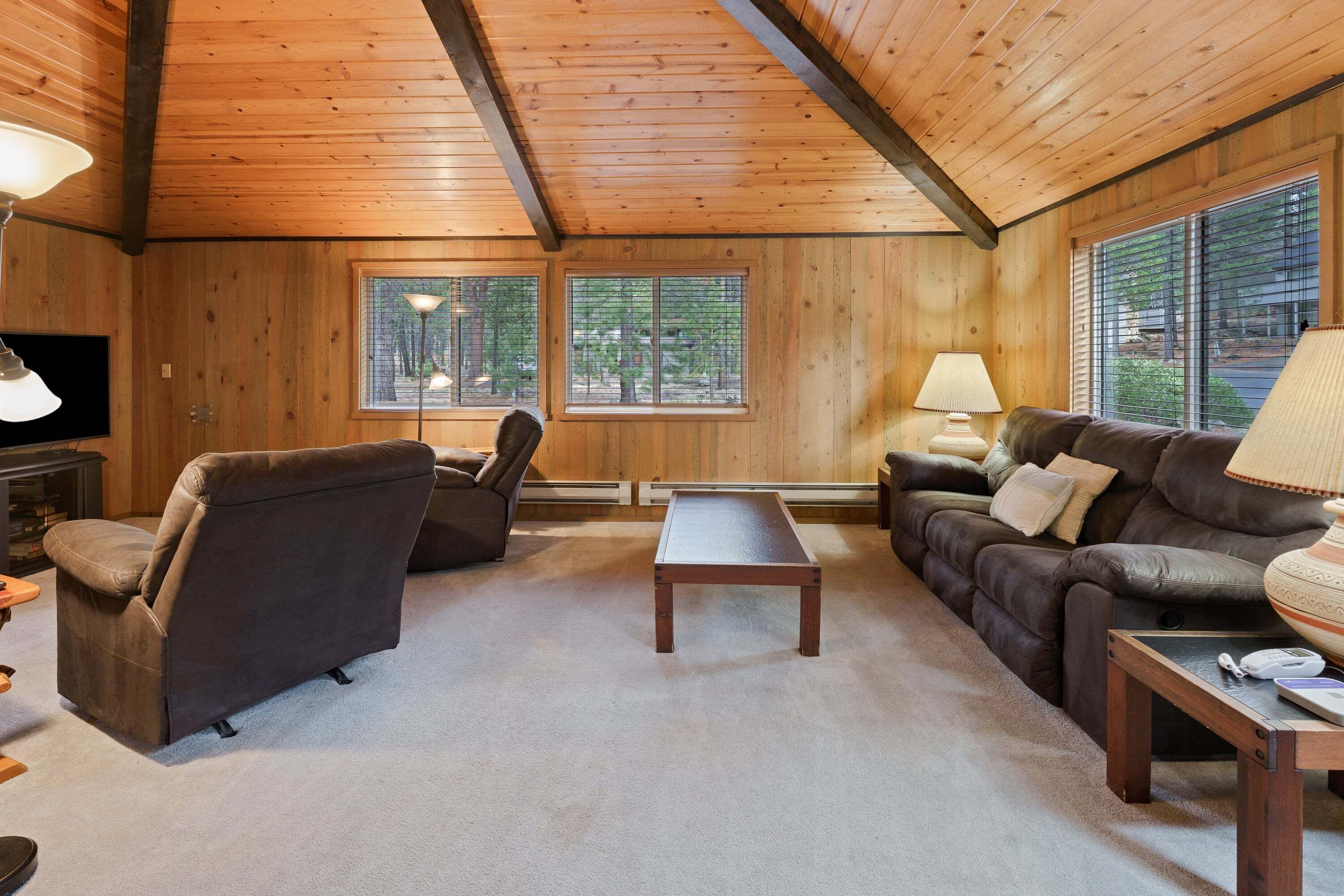 A cozy living room with wooden walls, a sofa, a chair, a coffee table, and a television.