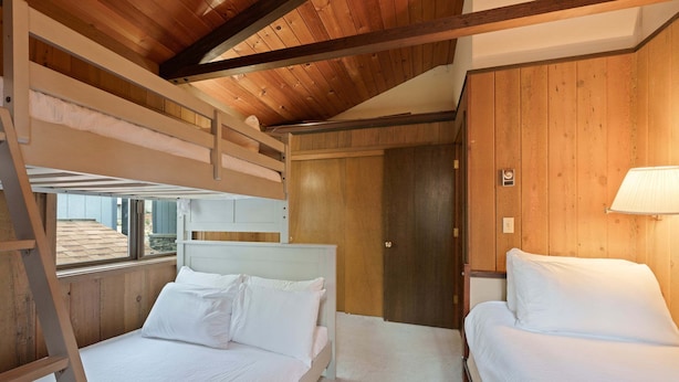Una habitación con dos camas, paredes de madera, una puerta y una ventana.