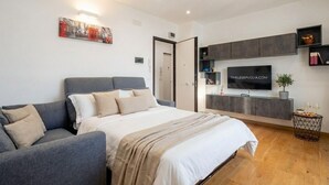 A modern bedroom with a bed, a grey sofa, a TV, and a small side table. - Sparano mood 170 - central cozy stay (Bari)