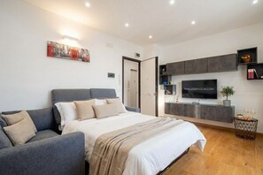 A modern bedroom with a bed, a grey sofa, a TV, and a small side table. - Sparano mood 170 - central cozy stay (Bari)