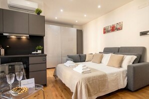 A modern hotel room with a bed, a sofa, a kitchen area, and a dining table with glasses and cookies. - Sparano mood 170 - central cozy stay (Bari)