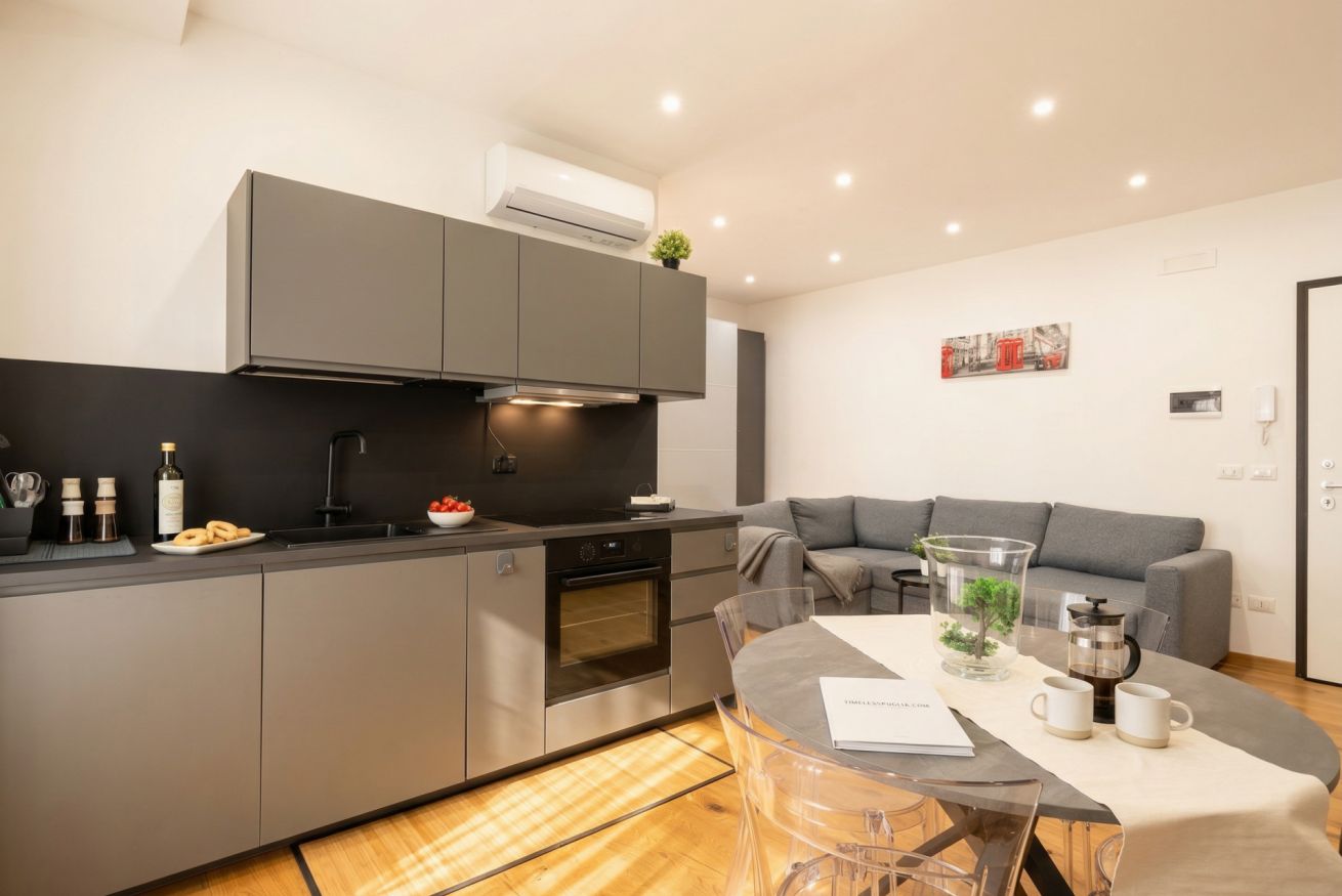 A modern kitchen with grey cabinetry, a built-in oven, and a dining area with a glass table.