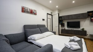 A modern hotel room with a grey sofa, a bed with white linens, a flat-screen TV, and a small cactus on the shelf. - Sparano mood 170 - central cozy stay (Bari)