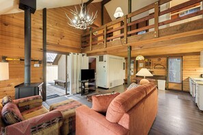 A spacious living area with a fireplace, a television, and a high ceiling with wooden beams.