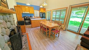 A kitchen with wooden cabinets, a stone fireplace, and a dining area with a table and chairs. - Circle Four Condo 14 - Hot Tub, SHARC Passes, Community Pool (Sunriver)