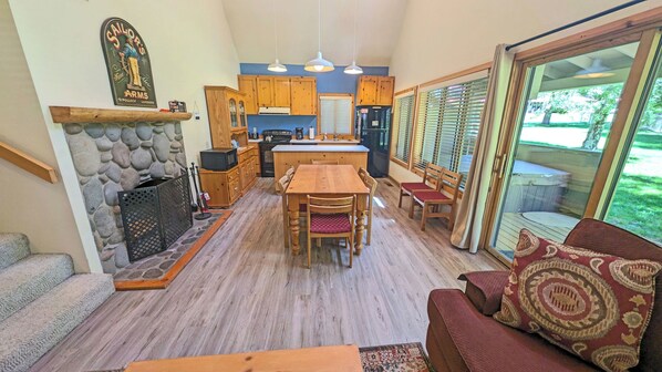 A cozy interior with a stone fireplace, wooden dining table, and a large window with blinds. - Circle Four Condo 14 - Hot Tub, SHARC Passes, Community Pool (Sunriver)