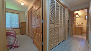 A bedroom with a bed, a wooden wardrobe, a window with blinds, and a bathroom with a sink and mirror. - Circle Four Condo 14 - Hot Tub, SHARC Passes, Community Pool (Sunriver)