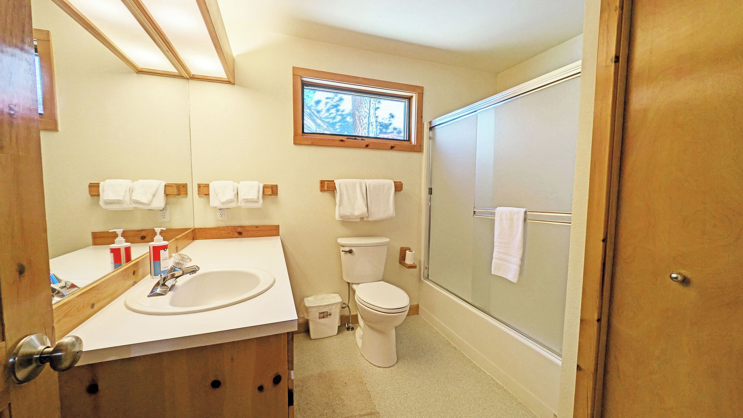 A bathroom with a sink, toilet, and shower. There are towels hanging on the wall and a window above the toilet.