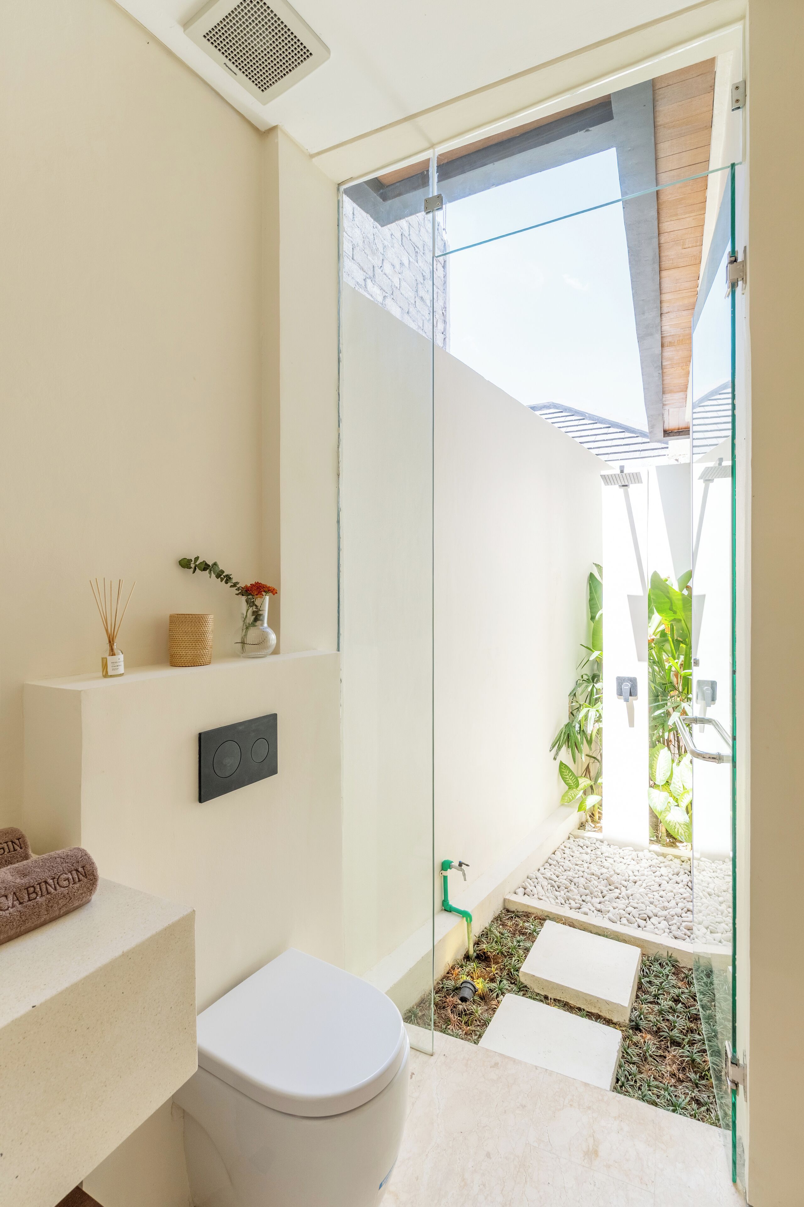 Une salle de bain moderne avec une douche à parois de verre, des toilettes, un lavabo avec une serviette et une petite étagère ornée d’objets décoratifs.