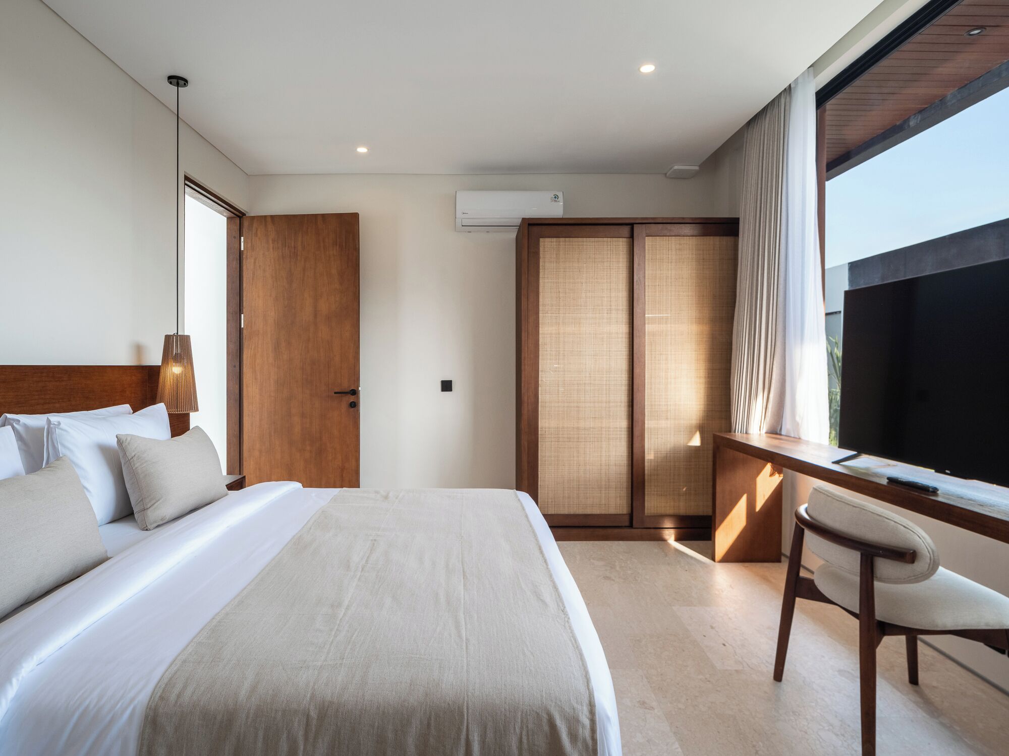 Una habitación de hotel moderna con una cama grande, un escritorio y una silla. Hay una ventana con cortinas y un equipo de aire acondicionado en la pared.