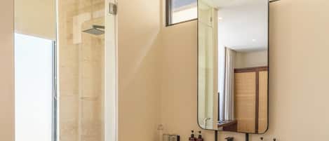 A modern bathroom with a glass shower enclosure, a large mirror, and a vanity with toiletries.
