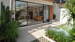 A modern house with a stone facade, large glass windows, and a patio area with plants and a pool. - La Finca Bingin (Pecatu)