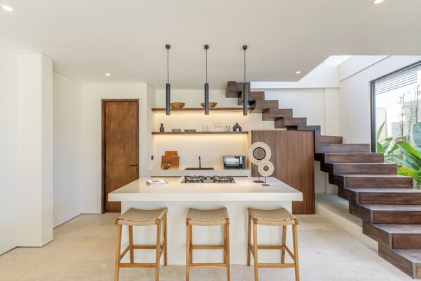 Une cuisine moderne dotée d’un îlot central, de tabourets de bar, de luminaires suspendus et d’un escalier menant à une mezzanine.