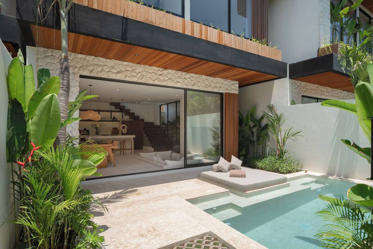 A modern house with a large glass window, a pool, and a staircase leading to a second floor.