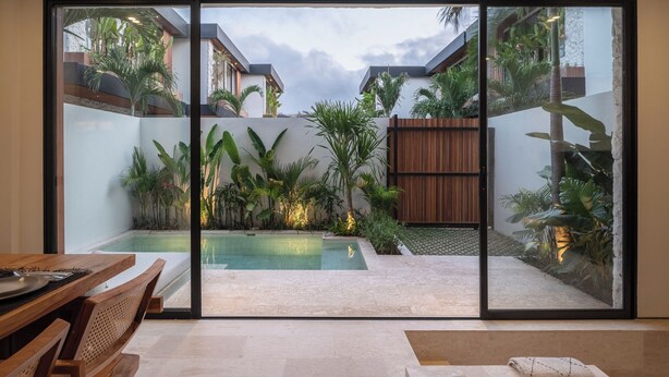 A modern outdoor patio with a swimming pool, surrounded by lush tropical plants and a wooden fence. - La Finca Bingin (Pecatu)